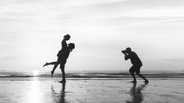 A Photographer is taking a picture of a couple on the beach