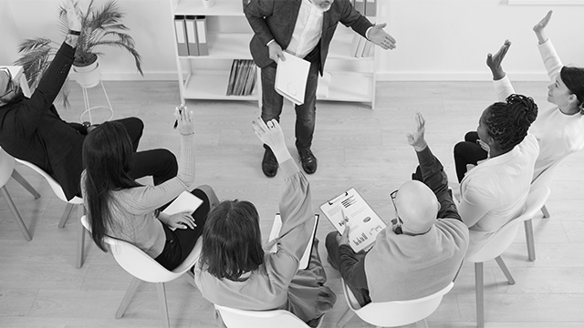 professional coach engaging the team and employees sitting in chairs and raising their hands to answer the question