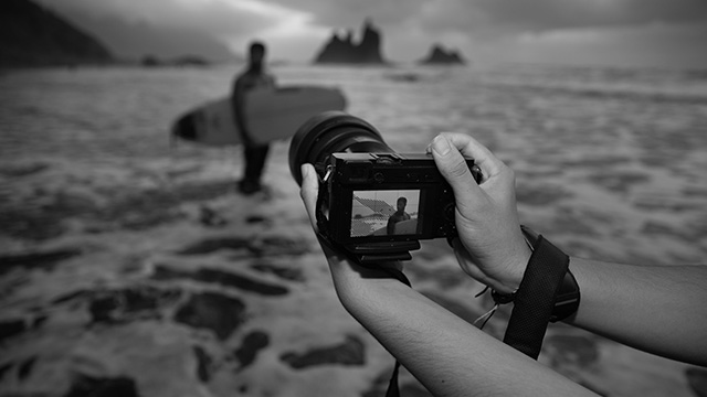 A close-up of a photographer's hand who is taking a picture of a model on a beach